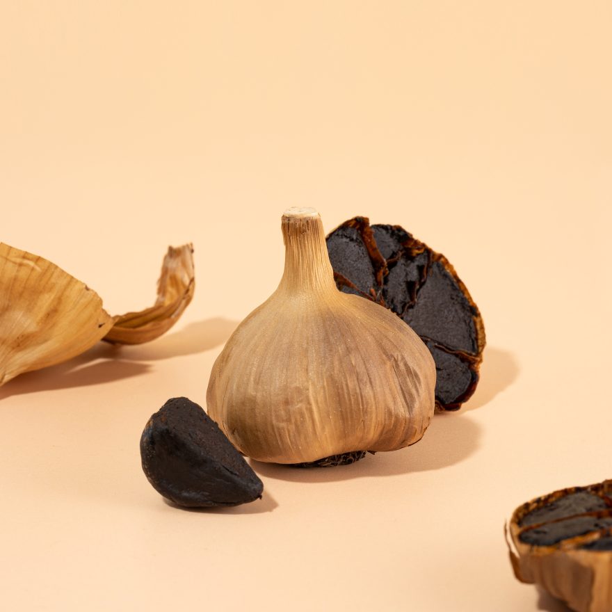 Black Garlic Bulbs, Cloves And Peel Lie On A Beige Table. A Conceptual Composition Of Healthy Food. Fermented Food, Vegetarian Food, Self Care, Healthy Nutrition